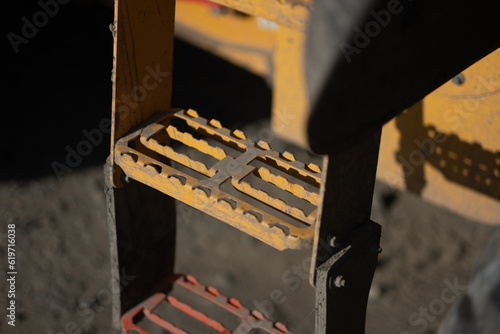 Steel ladder into the operator cab of a heavy machine at a busy construction site. The steps are grated, allowing dirt and debris to fall through unimpeded.  photo
