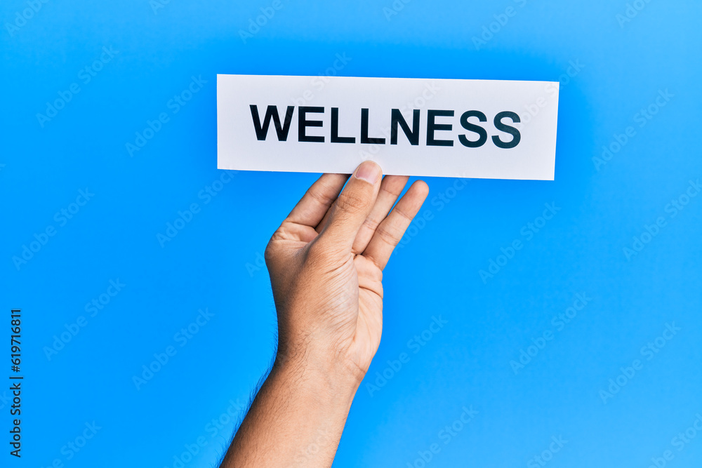 Hand of caucasian man holding paper with wellness word over isolated blue background Hand of caucasian man holding paper with wellness word over isolated blue background