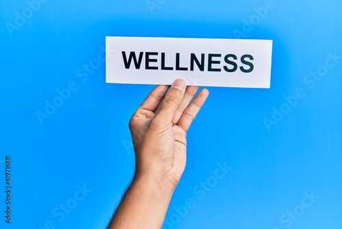 Hand of caucasian man holding paper with wellness word over isolated blue background