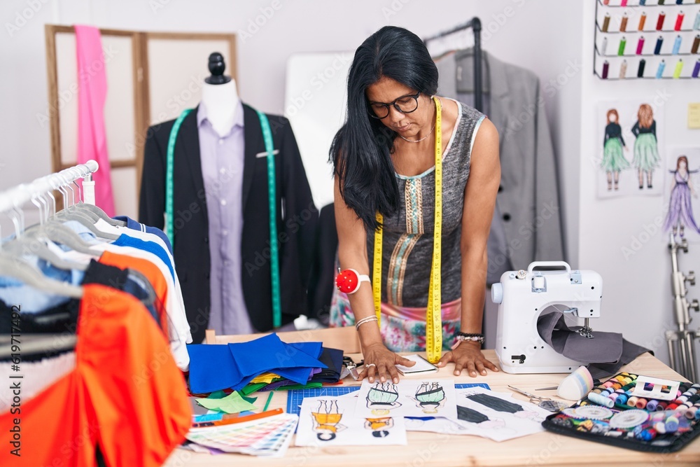 Middle age hispanic woman tailor looking clothing design at tailor shop Middle age hispanic woman tailor looking clothing design at tailor shop