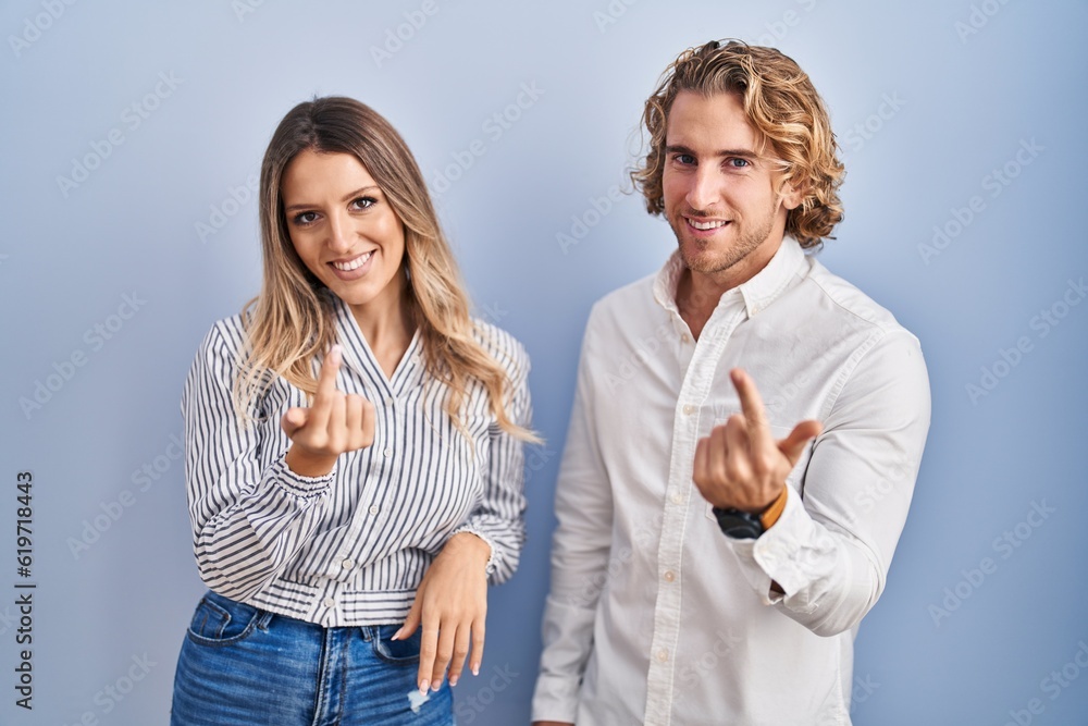 Young couple standing over blue background beckoning come here gesture with hand inviting welcoming happy and smiling Young couple standing over blue background beckoning come here gesture with hand inviting welcoming happy and smiling