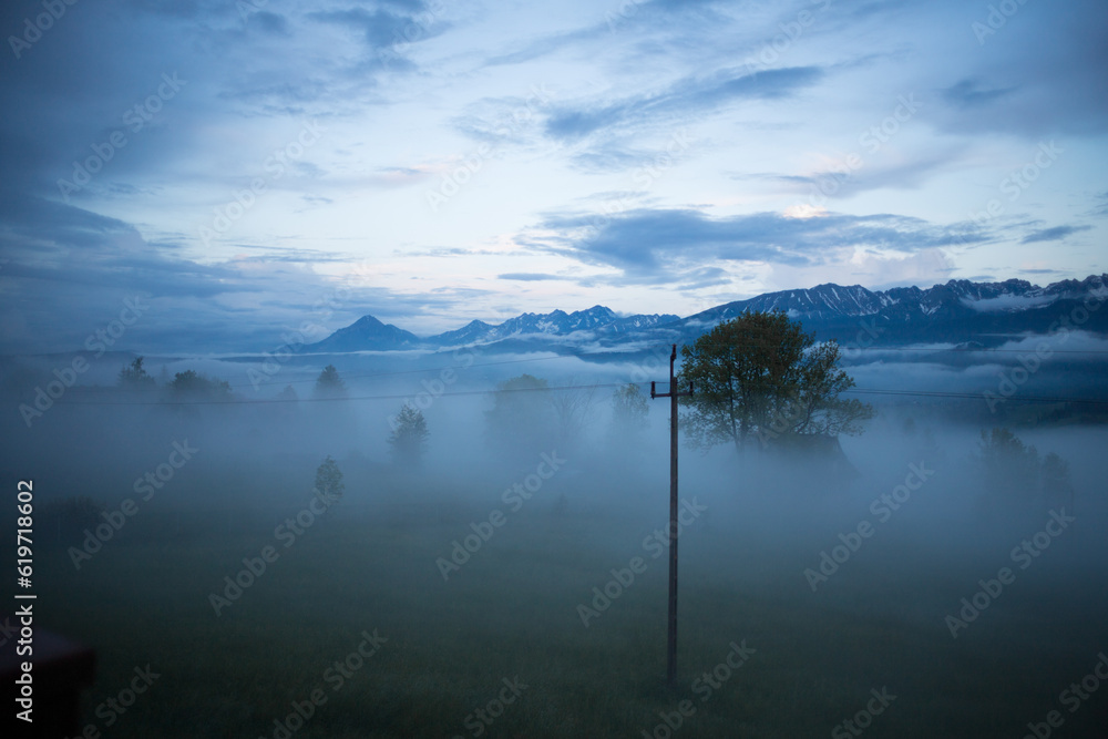 Cloudy weather in the mountains. Tatras in clouds and fog. Clouds float below the mountain peaks. Trees in the clouds. View from the height of the villa, located at an altitude of 1100 meters.