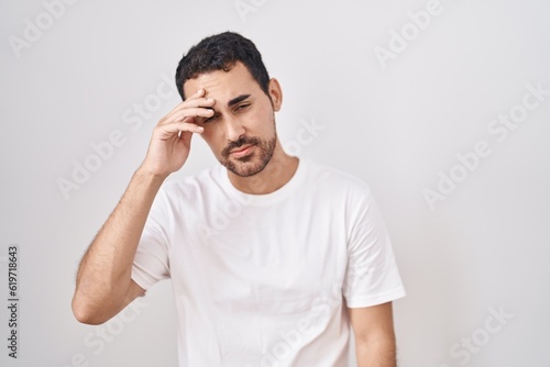 Handsome hispanic man standing over white background worried and stressed about a problem with hand on forehead, nervous and anxious for crisis