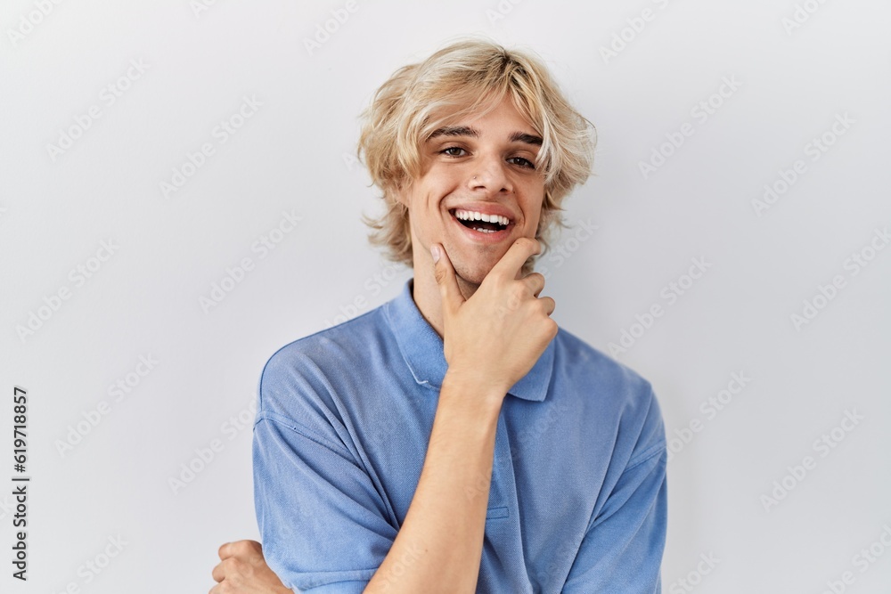 Young modern man standing over isolated background looking confident at the camera smiling with crossed arms and hand raised on chin. thinking positive. Young modern man standing over isolated background looking confident at the camera smiling with crossed arms and hand raised on chin. thinking positive.
