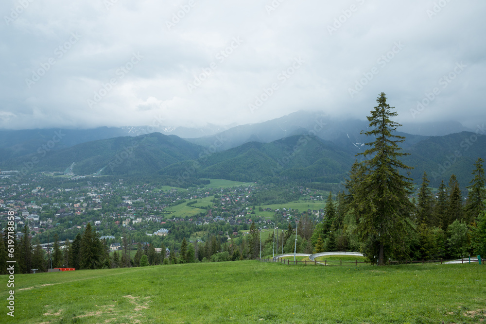 Mountain panorama. Mountain peaks in cloudy weather. Foggy mountain peaks and a city in the gorge between them. Tatras hanging over the city of Zakopane.