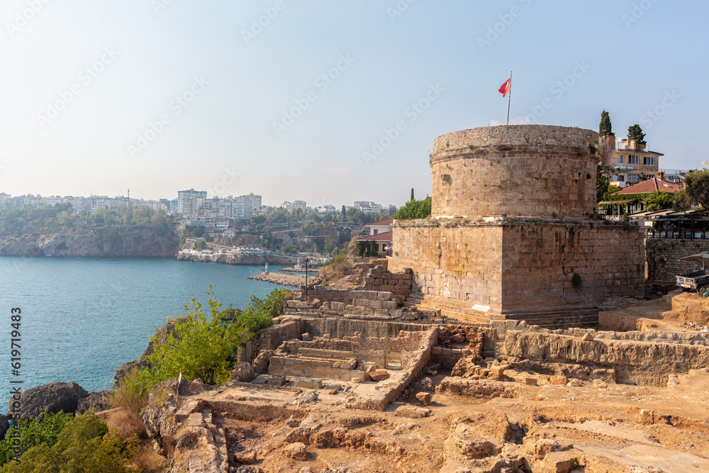 Hidirlik Tower, part of Roman fortress II cent AD with archaelogical excavations at forefround. Bay and the landscape of modern Antalya at background. Travel and history concept. Antalya, Turkey