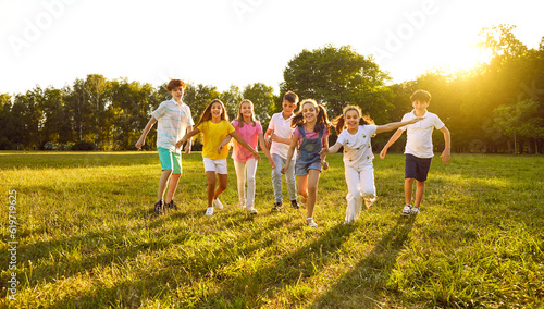 Happy children playing in the park in summer. Group of cheerful kid friends playing active outdoor games, running on a green grassy lawn, having fun and enjoying free time #619719625