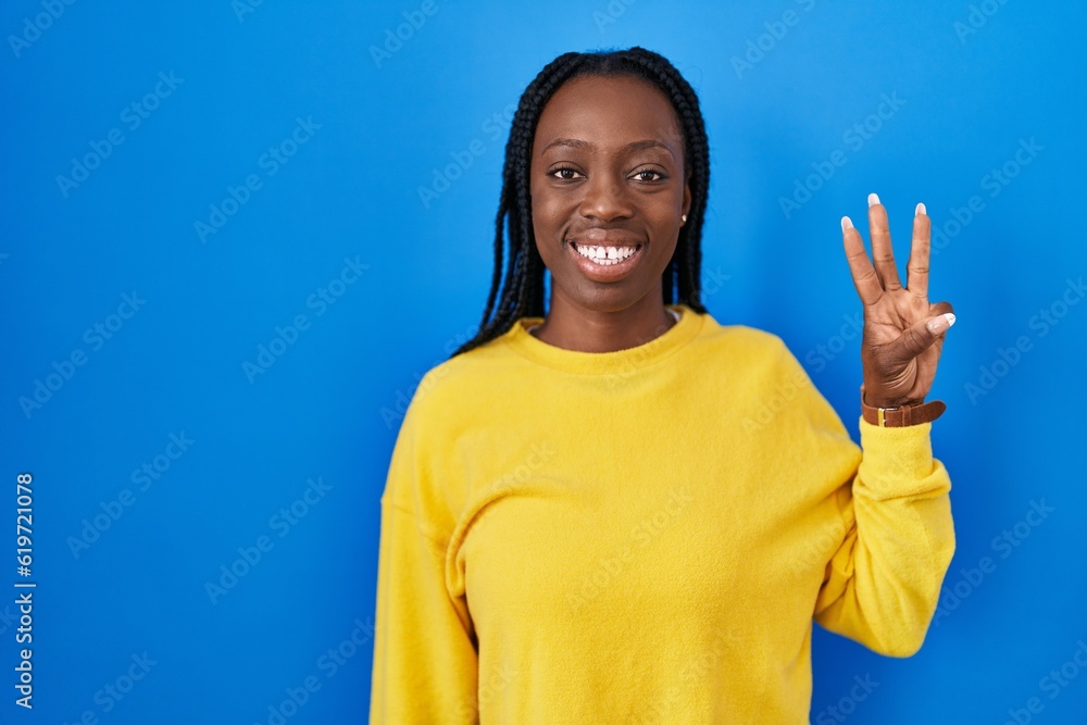 Beautiful black woman standing over blue background showing and pointing up with fingers number three while smiling confident and happy. Beautiful black woman standing over blue background showing and pointing up with fingers number three while smiling confident and happy.