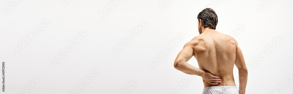 Horizontal banner with half-length portrait of shirtless man standing his back to camera. Man experiencing back pain.