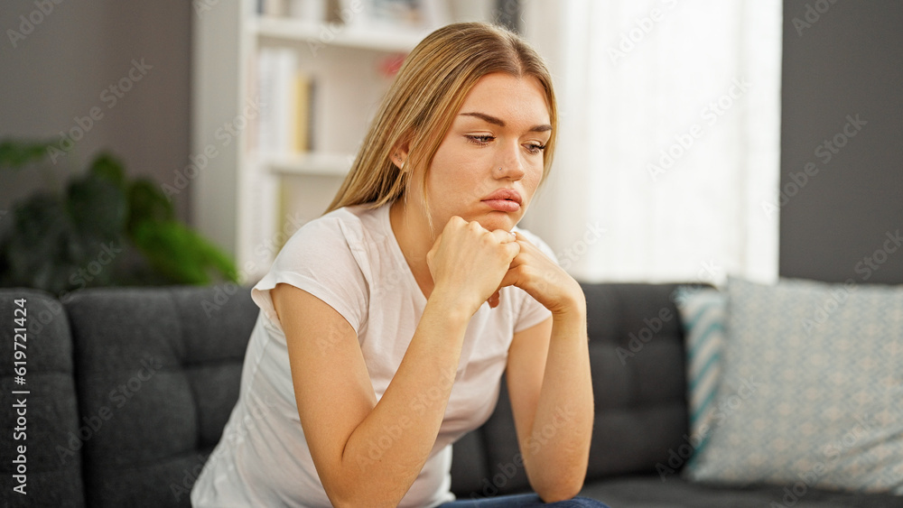 Young blonde woman sitting on sofa with serious expression at home Young blonde woman sitting on sofa with serious expression at home