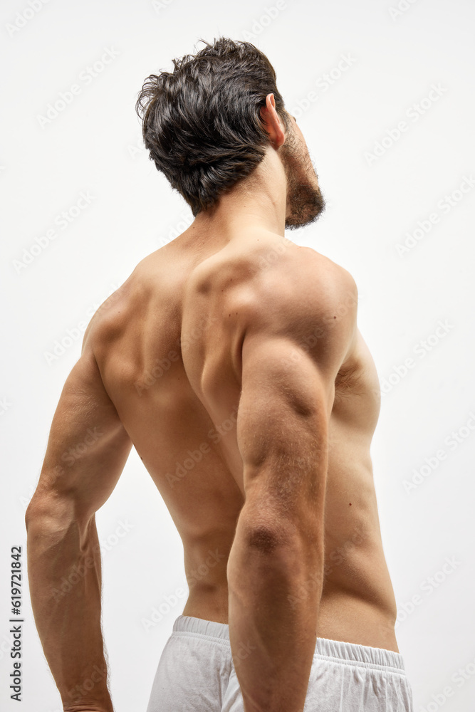 Back view of strong musculed young man posing topless over white background. Beauty, fashion, sport, fitness concept