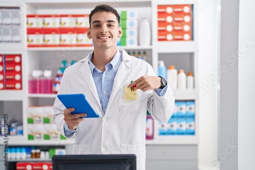 Handsome hispanic man working at pharmacy drugstore with tablet pointing finger to one self smiling happy and proud