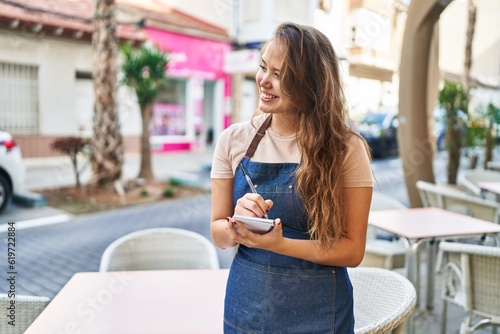 Young beautiful hispanic woman waitress smiling confident writing on notebook at coffee shop terrace © Krakenimages.com