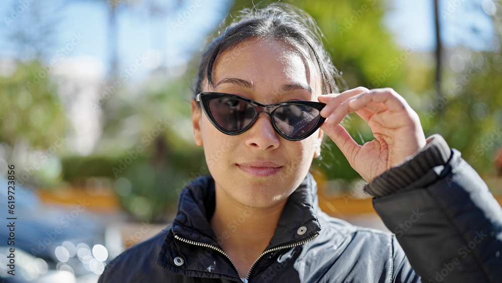 Young beautiful hispanic woman standing with serious expression wearing sunglasses at park Young beautiful hispanic woman standing with serious expression wearing sunglasses at park