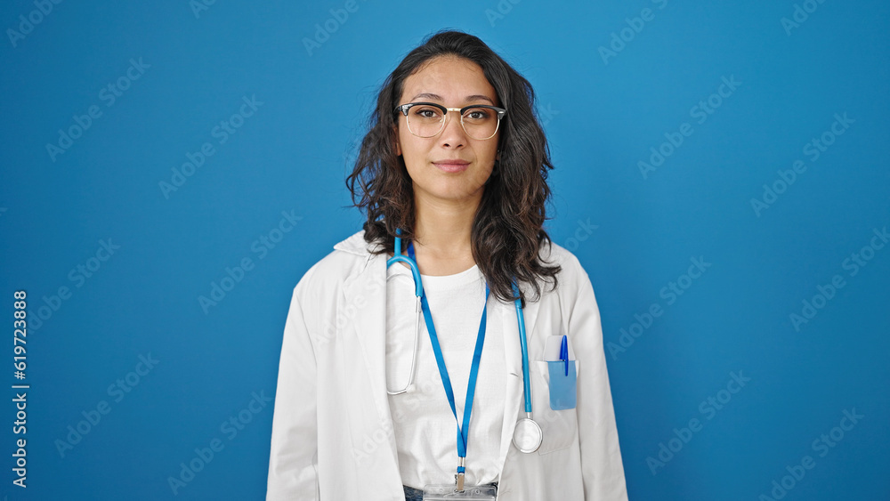 Young beautiful hispanic woman doctor standing with serious expression over isolated blue wall background Young beautiful hispanic woman doctor standing with serious expression over isolated blue wall background