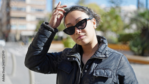 Young beautiful hispanic woman standing with serious expression wearing sunglasses at park
