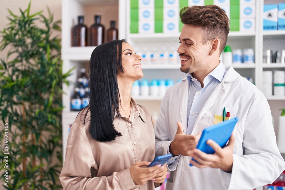 Man and woman pharmacist and client using smartphone and touchpad at pharmacy Man and woman pharmacist and client using smartphone and touchpad at pharmacy