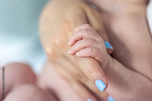 The small hand of a newborn holds the mother's finger.