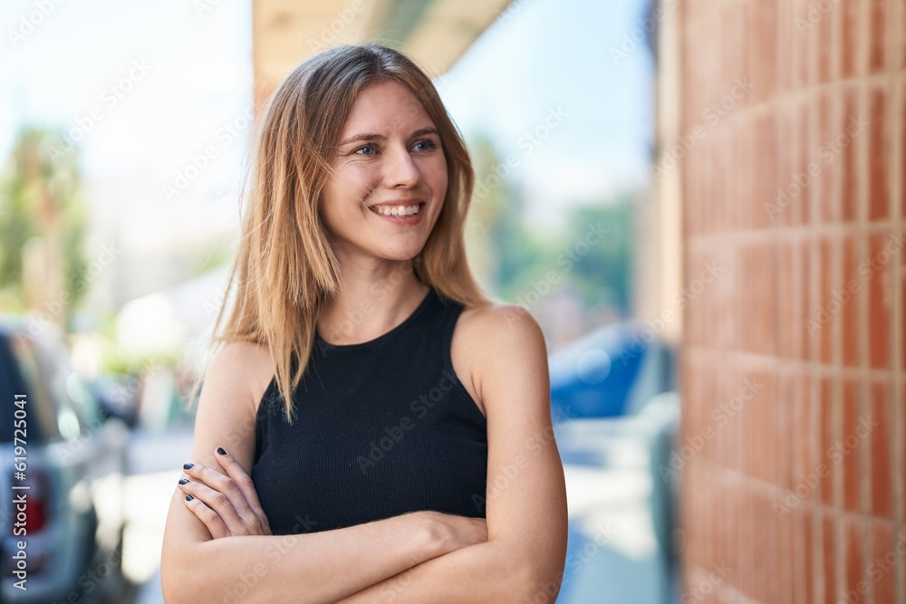 Young blonde woman standing with crossed arms looking to the side at street