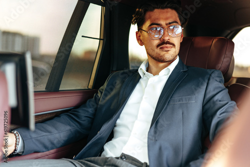 Young businessman in suit and glasses sitting on passenger seat in a luxury car