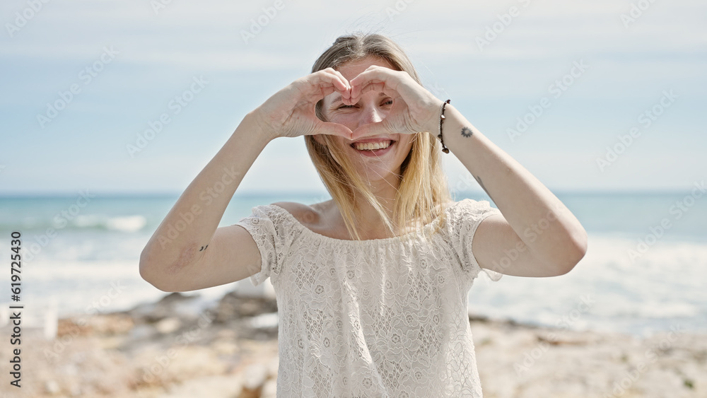 Young blonde woman tourist smiling confident doing heart gesture at beach Young blonde woman tourist smiling confident doing heart gesture at beach