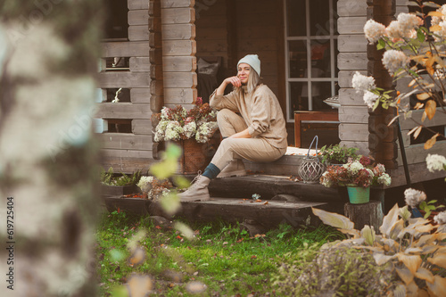 woman gardener relaxing in cozy autumn day, sitting on wooden stairs at house entryway. Enjoying warm october in the countryside, spending weekend outdoor