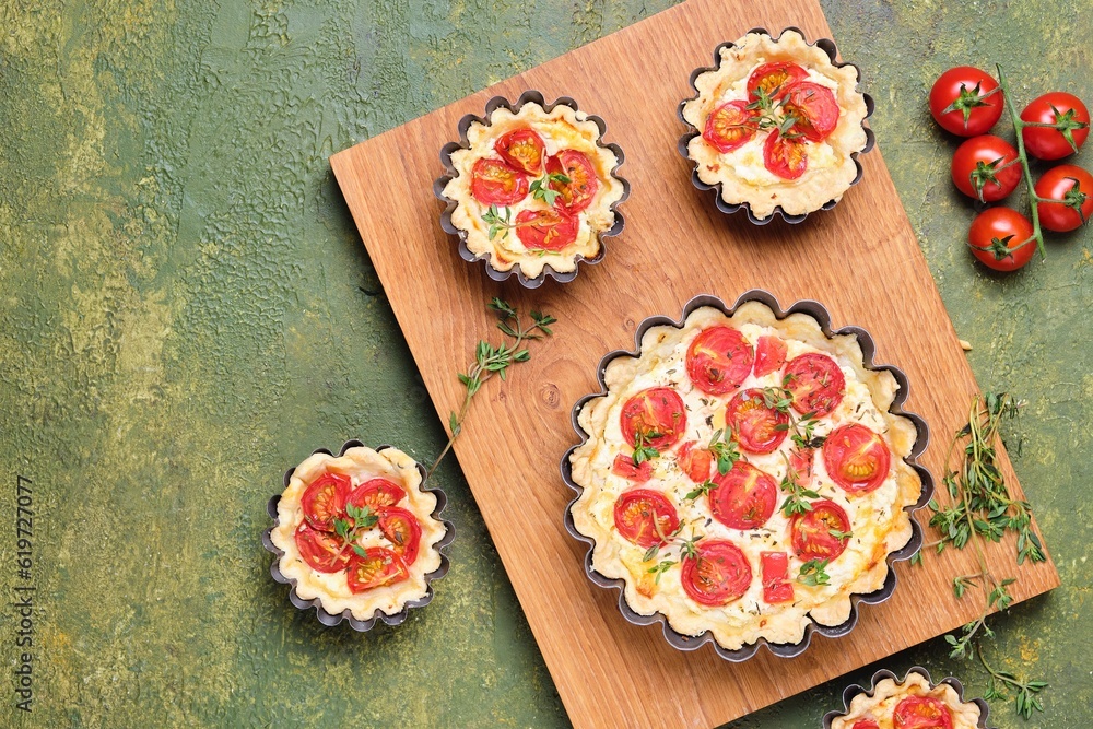 Unsweetened shortbread tartlets with feta cheese, cherry tomatoes and herbs on a wooden board on a green concrete background. Unsweetened pastries Unsweetened shortbread tartlets with feta cheese, cherry tomatoes and herbs on a wooden board on a green concrete background. Unsweetened pastries