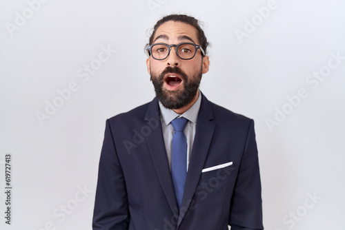 Hispanic man with beard wearing suit and tie afraid and shocked with surprise expression, fear and excited face.