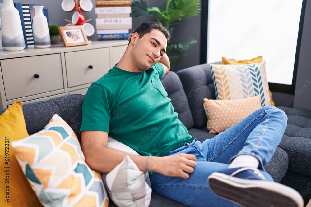Obraz premium Young hispanic man relaxed with hand on head sitting on sofa at home