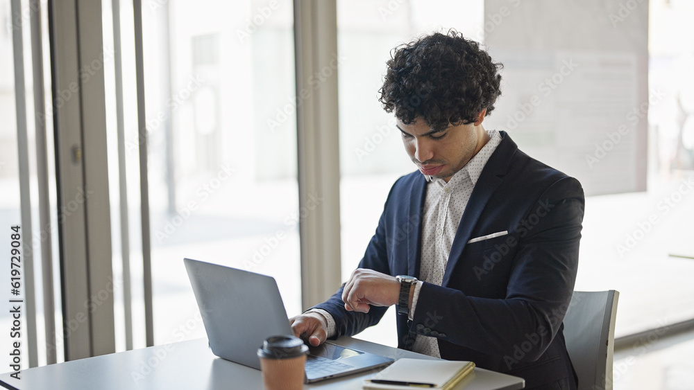 Young latin man business worker using laptop looking watch at office Young latin man business worker using laptop looking watch at office