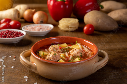 Meatballs soup with noodles and vegetables, romanian traditional food. wooden background. Ciorba de perisoare.