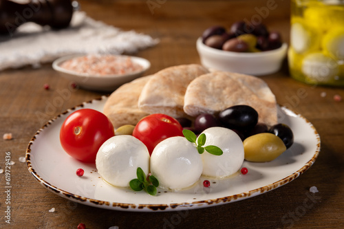 Labneh - yogurt balls with tomatoes, olives, pita and oregano on wooden background.