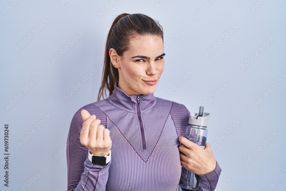 Beautiful woman wearing sportswear holding water bottle doing money gesture with hands, asking for salary payment, millionaire business Beautiful woman wearing sportswear holding water bottle doing money gesture with hands, asking for salary payment, millionaire business