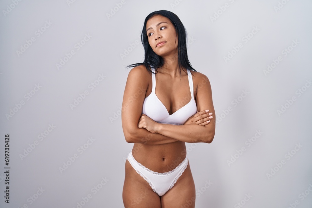 Fototapeta premium Hispanic woman wearing lingerie looking to the side with arms crossed convinced and confident