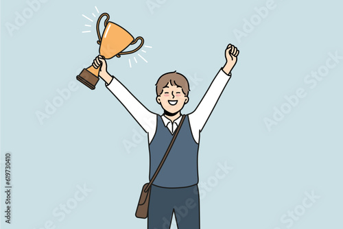 Schoolboy with golden cup rejoices at award received for winning school mathematics olympiad. Schoolboy with trophy makes winning gesture demonstrating leadership qualities while receiving education