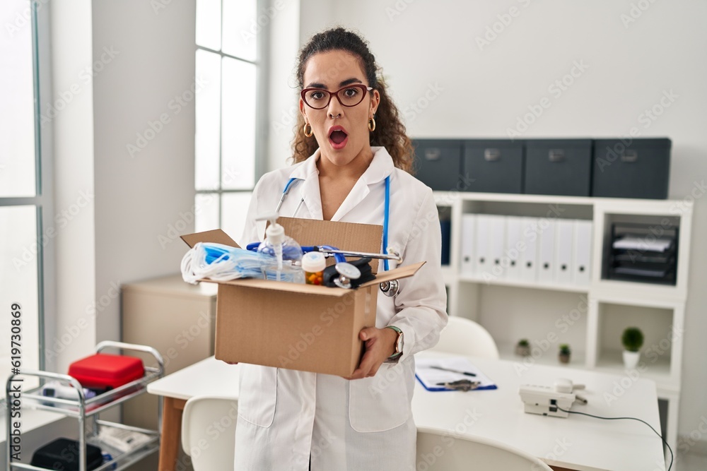 Young hispanic woman holding box with medical items afraid and shocked with surprise and amazed expression, fear and excited face. Young hispanic woman holding box with medical items afraid and shocked with surprise and amazed expression, fear and excited face.