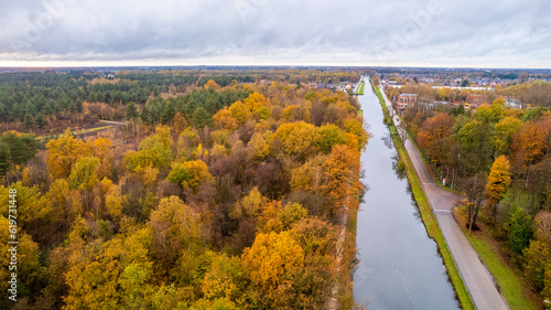 Immerse yourself in the vibrant tapestry of autumn as the camera captures an enchanting aerial view of a river or canal flowing through the woods, adorned with colorful fall foliage, all set against a