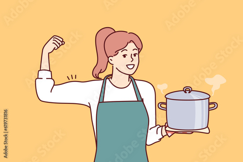 Woman cook holds pot of soup and shows biceps as sign of pride in ability to cook complex dish. Girl housewife in apron smiles inviting to eat delicious homemade food from healthy ingredients