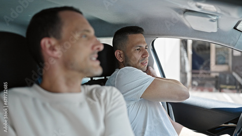 Two men couple sitting on car wearing belt at street