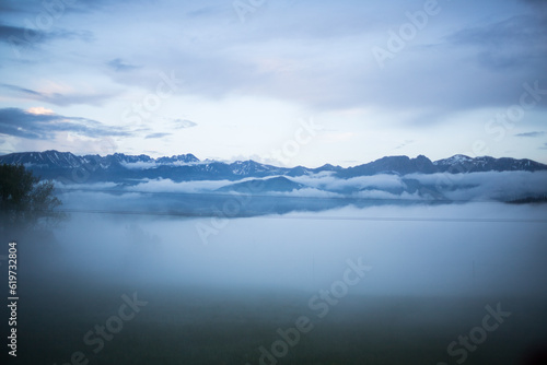 Cloudy weather in the mountains. Panorama of the mountain range. Floating clouds. View of the mountains through the clouds. Closed peaks of the mountain range. Bird's-eye view.