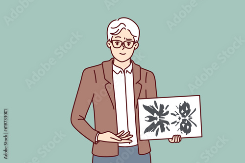 Man psychotherapist holds picture of rorschach test to determine patient personality type. Elderly psychotherapist demonstrates piece of paper with blots for medical psychiatric experiment.