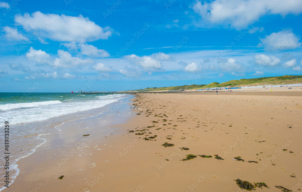 Sand beach along a sea under a dark blue cloudy sky in bright sunlight in summer, Zeeland, the Netherlands, June, 2023 Sand beach along a sea under a dark blue cloudy sky in bright sunlight in summer, Zeeland, the Netherlands, June, 2023