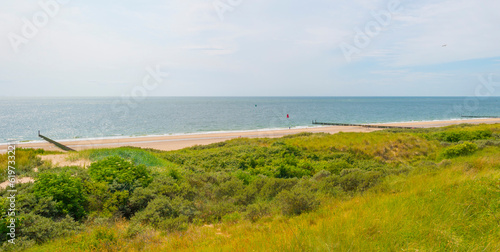 Sand beach along a sea under a dark blue cloudy sky in bright sunlight in summer, Zeeland, the Netherlands, June, 2023