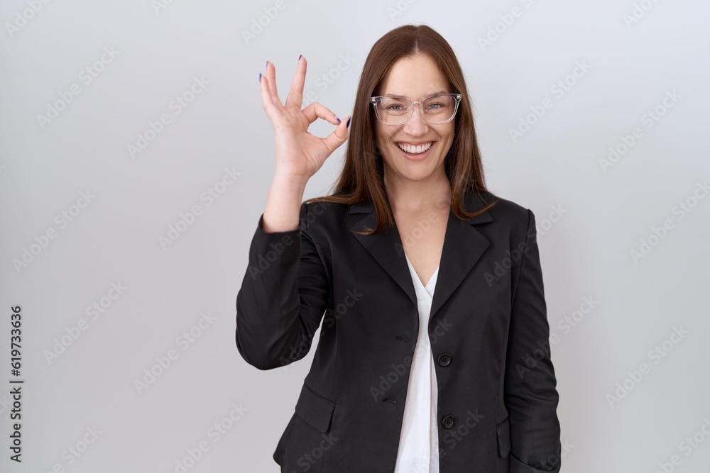 Beautiful brunette woman wearing business jacket and glasses smiling positive doing ok sign with hand and fingers. successful expression. Beautiful brunette woman wearing business jacket and glasses smiling positive doing ok sign with hand and fingers. successful expression.