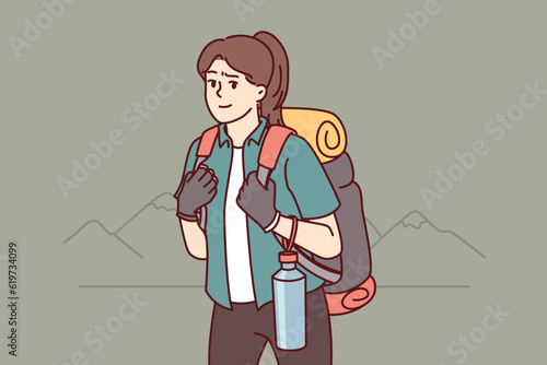 Woman tourist returns from hiking with large backpack on back and bottle of water posing near mountains. Girl is fond of hiking and loves to travel to natural parks and national reserves