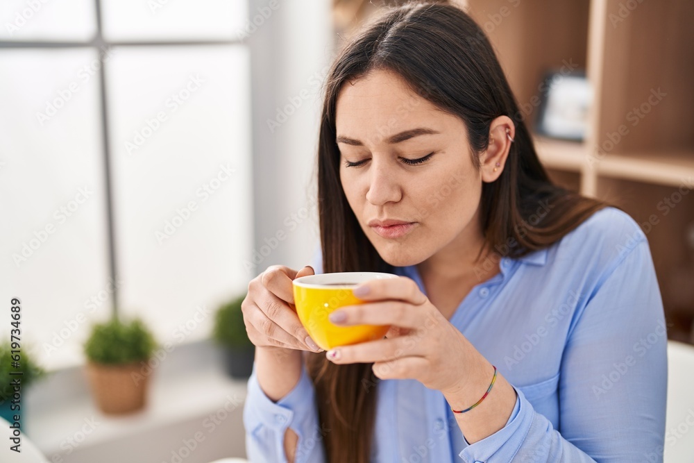 Young woman smelling cup of coffee sitting on table at home Young woman smelling cup of coffee sitting on table at home