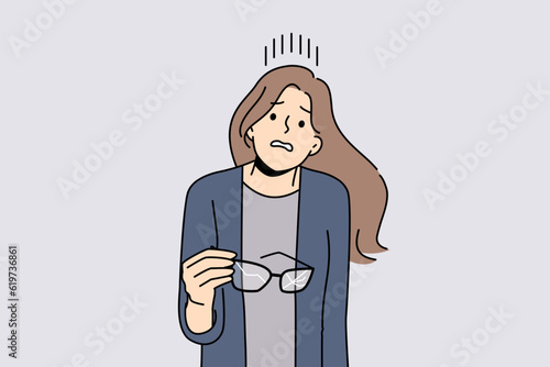 Woman with broken glasses in hands makes confused face not knowing how to solve vision problem. Careless girl holds glasses with cracked glass and needs to go to optometrist or buy contact lenses