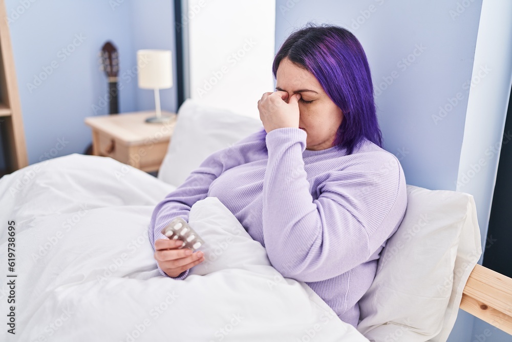 Young beautiful plus size woman taking pills for headache sitting on bed at bedroom Young beautiful plus size woman taking pills for headache sitting on bed at bedroom