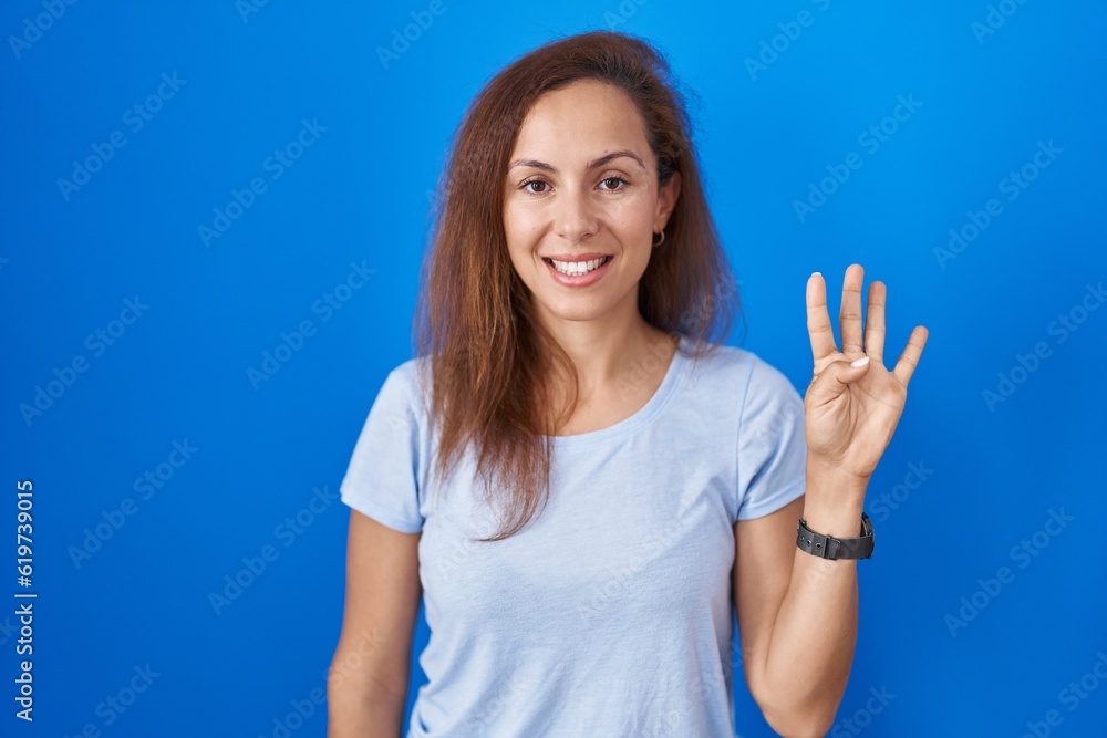 Fototapeta premium Brunette woman standing over blue background showing and pointing up with fingers number four while smiling confident and happy.