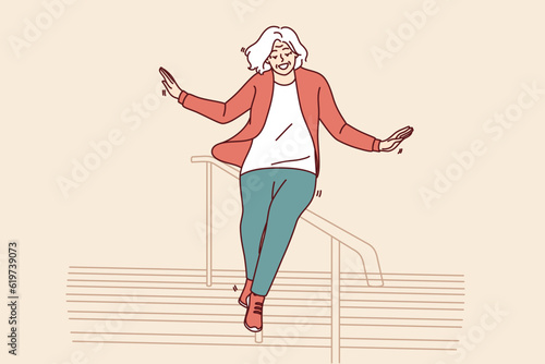 Elderly woman slides down stair railing having fun and being active after retirement. Cheerful elderly woman in casual clothes feels full of energy and laughs regardless of mature age